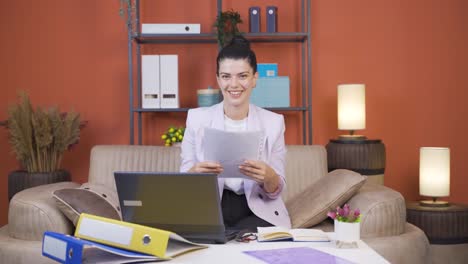 Home-office-worker-young-woman-smiling-at-camera-looking-at-paperwork.